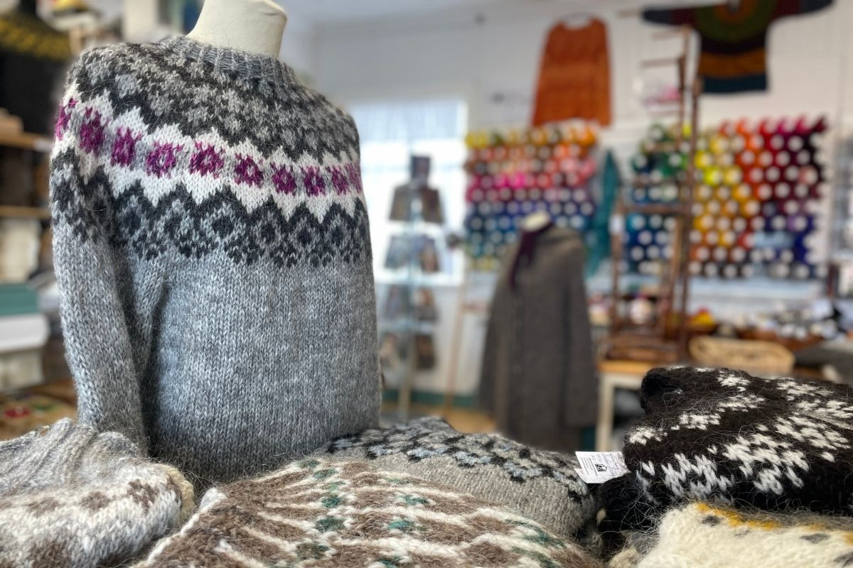 A display of traditional Icelandic lopapeysa sweaters, with one on a mannequin featuring a gray and white pattern with a vibrant purple design, and several others folded on a table in the foreground.