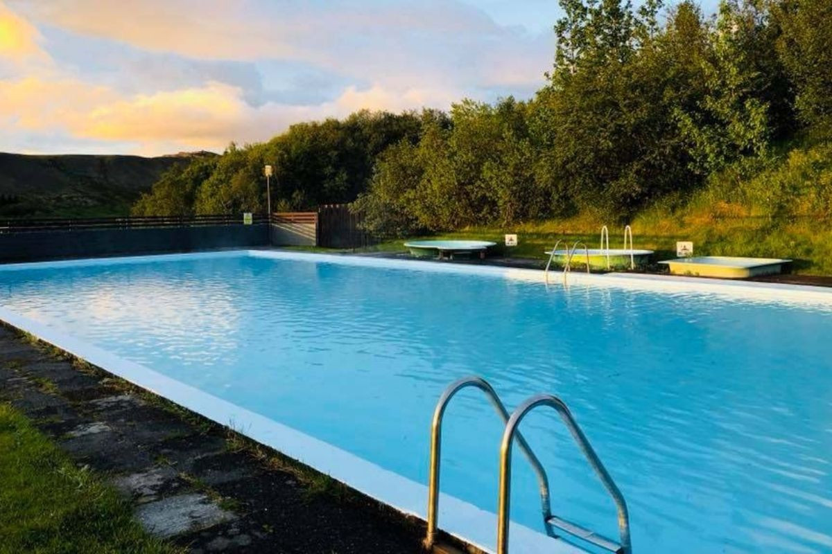 An outdoor view of the Hreppslaug thermal pool in Iceland, surrounded by greenery under a partly cloudy sky.