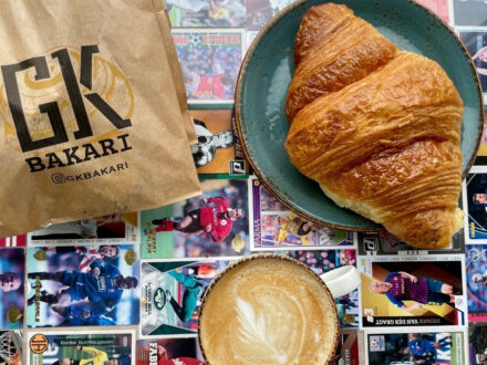 Croissant, coffee, and a GK Bakari paper bag on a table covered with sports trading cards.