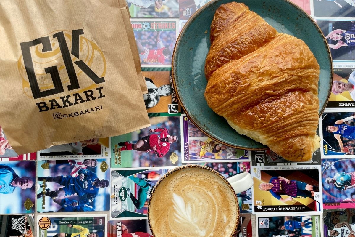 Croissant, coffee, and a GK Bakari paper bag on a table covered with sports trading cards.