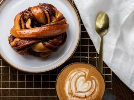 A delicious cinnamon bun on a plate next to a latte with latte art at Hygge Coffee and Micro Bakery in Reykjavik.