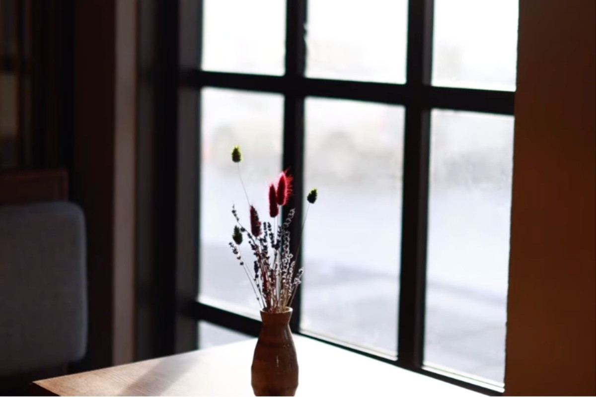 A charming table setting by the window at Hygge Coffee and Micro Bakery in Reykjavik, featuring a small vase with dried flowers.