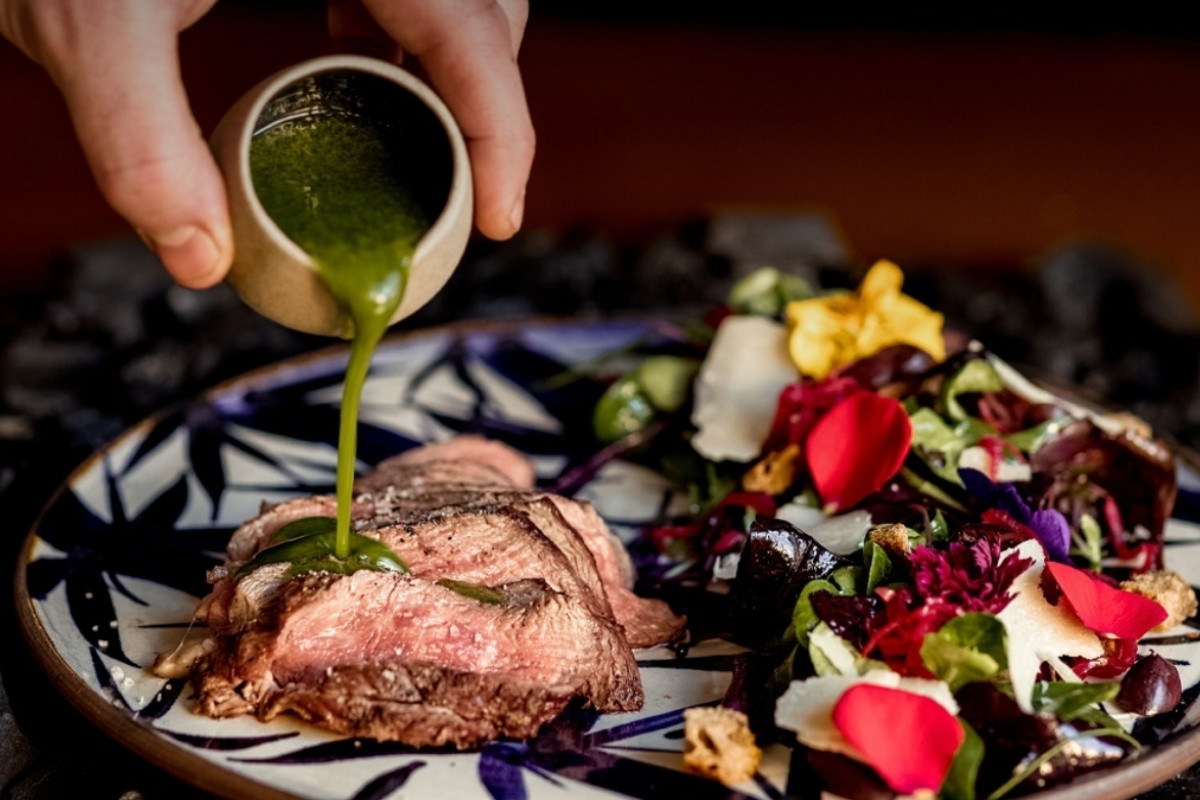 A beautifully presented dish at Kol Restaurant in Reykjavik, featuring a lamb steak with a vibrant green sauce being poured over it, accompanied by a colorful salad.