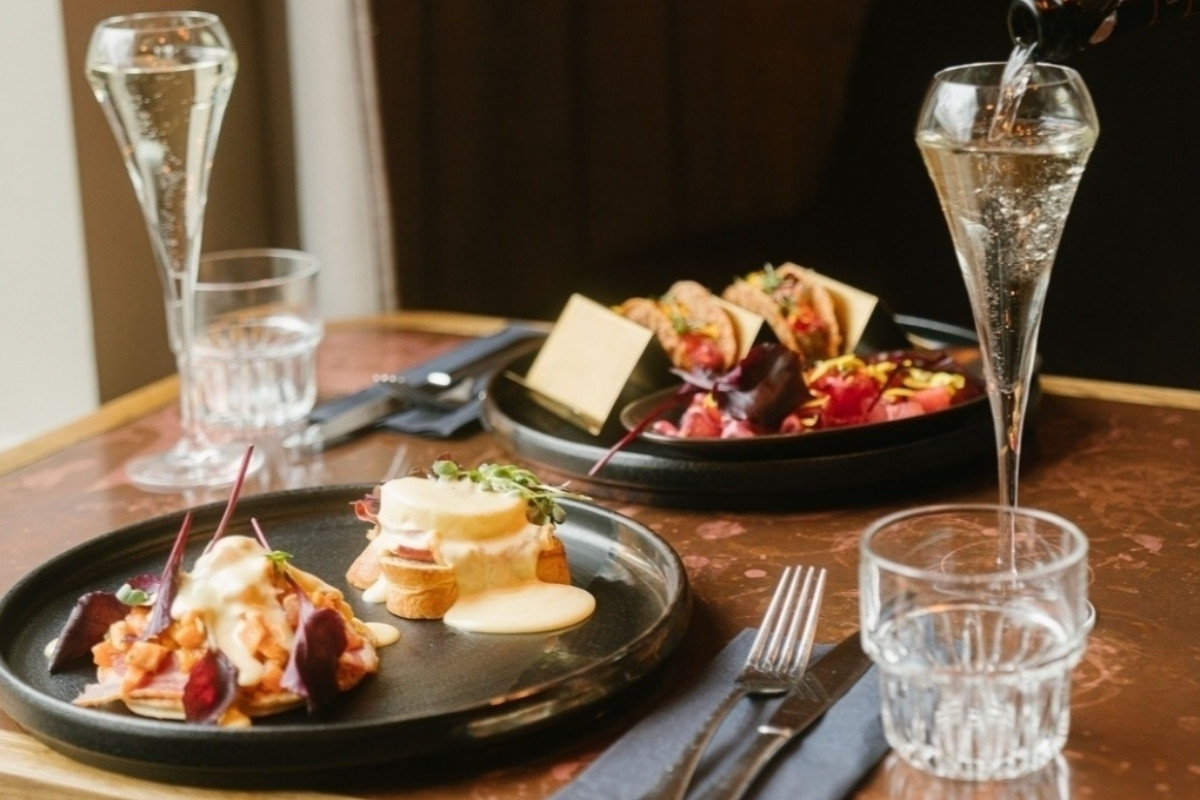 A table at Kol Restaurant in Reykjavik set with plates of brunch dishes, including eggs benedict and small tacos, with champagne being poured into a glass.