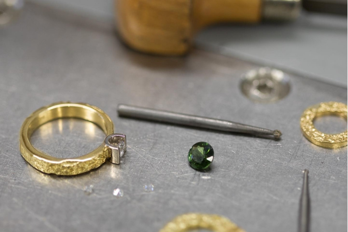 A close-up of the jewellery making process, showing a gold ring, a green gemstone, and tools at Prakt Jewellery.