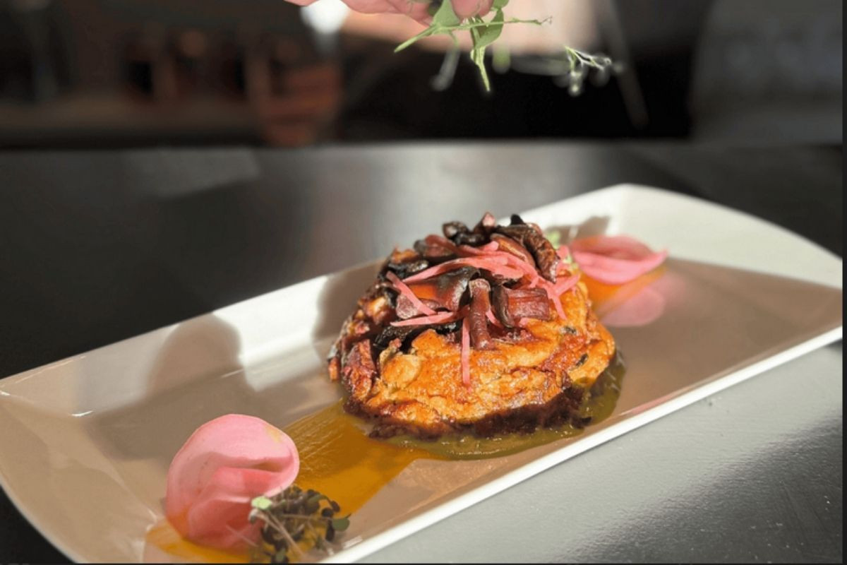 An artfully presented mushroom tart with garnishes and sauce, being finished by a chef at Torfan Restaurant.