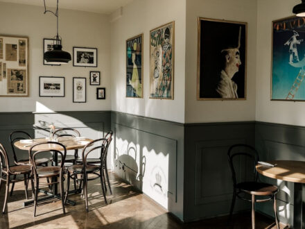 Interior view of Jomfruin restaurant in Reykjavik, featuring wooden tables and chairs, and framed artwork on the white and gray paneled walls.