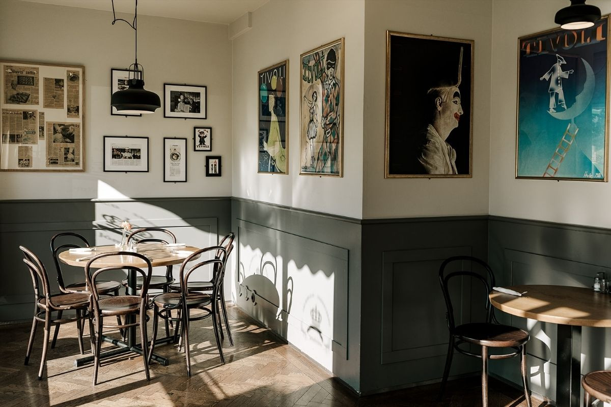 Interior view of Jomfruin restaurant in Reykjavik, featuring wooden tables and chairs, and framed artwork on the white and gray paneled walls.