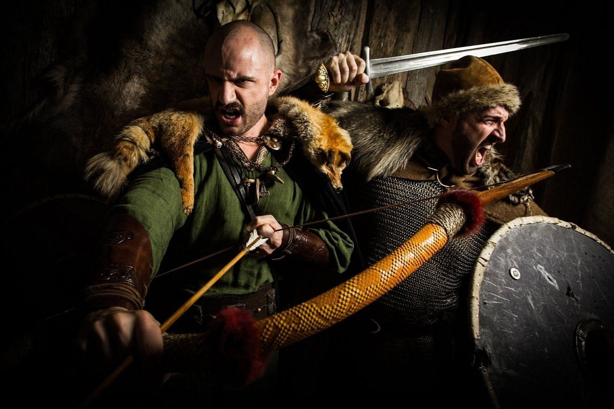 Two men in Viking-era costumes, one drawing a bow and arrow and the other wielding a sword and shield, at Mink Viking Portrait in Reykjavik.