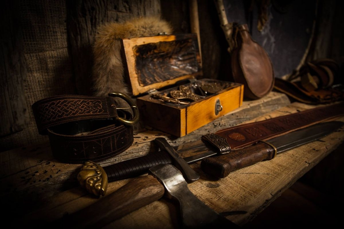 A collection of Viking-style weapons and accessories on a wooden surface at Mink Viking Portrait in Reykjavik, including a sword, axe, belt, and chest.