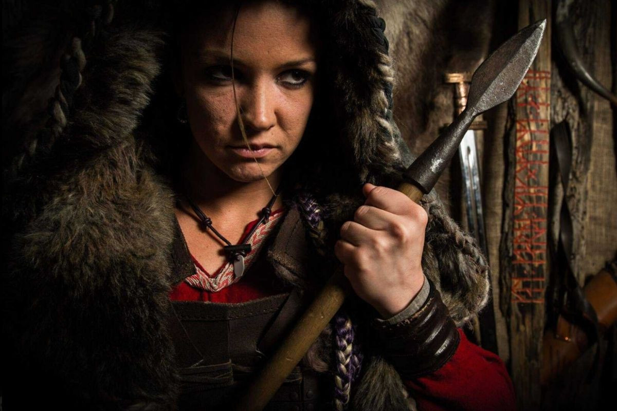 A close-up portrait of a woman dressed as a Viking warrior holding a spear, wearing fur and leather garments, at Mink Viking Portrait in Reykjavik.