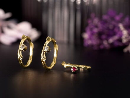 .Handcrafted gold rings with diamonds and ruby by Prakt Jewelry, displayed against a dark floral background in Reykjavik.