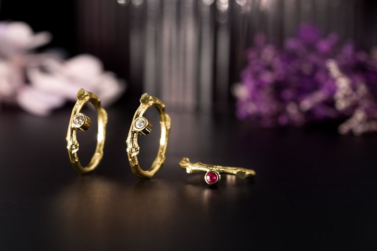 .Handcrafted gold rings with diamonds and ruby by Prakt Jewelry, displayed against a dark floral background in Reykjavik.