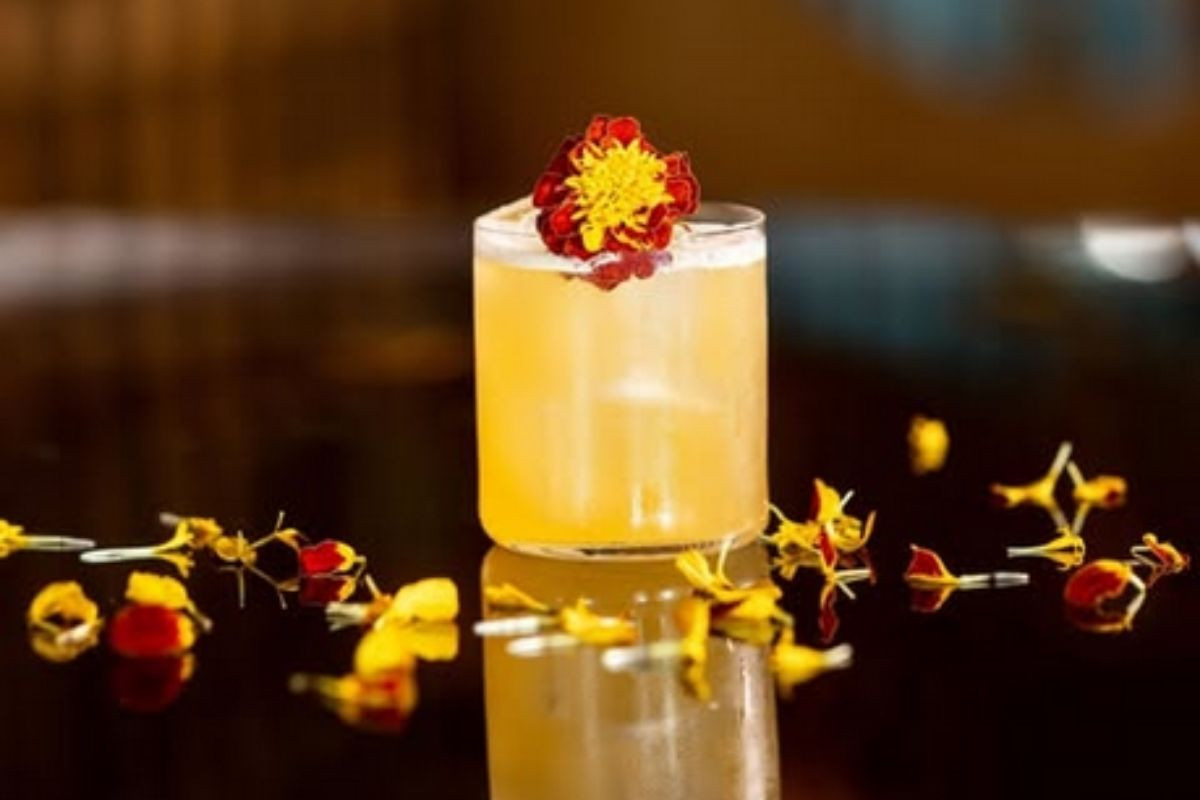 Elegant floral cocktail from Monkeys Restaurant in Reykjavik, garnished with edible red and yellow flowers on a black reflective surface.