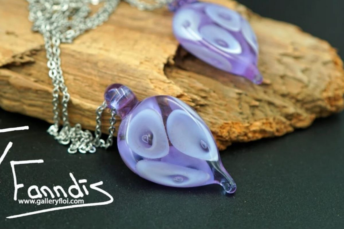 Handcrafted Droplaug hálsmen D. Lavender pendants from Gallery Flói in Iceland, showcasing intricate purple and white patterns on a rustic wooden base.