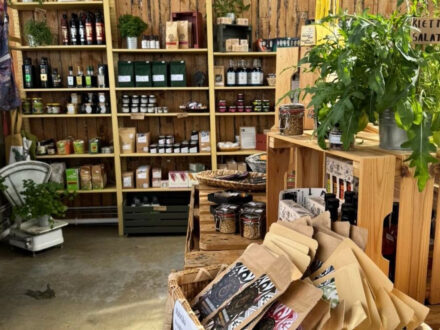 A vibrant display of organic and locally sourced products at Sólskinsbúðin, including bottled oils, packaged foods, and fresh greens, arranged on wooden shelving and crates.