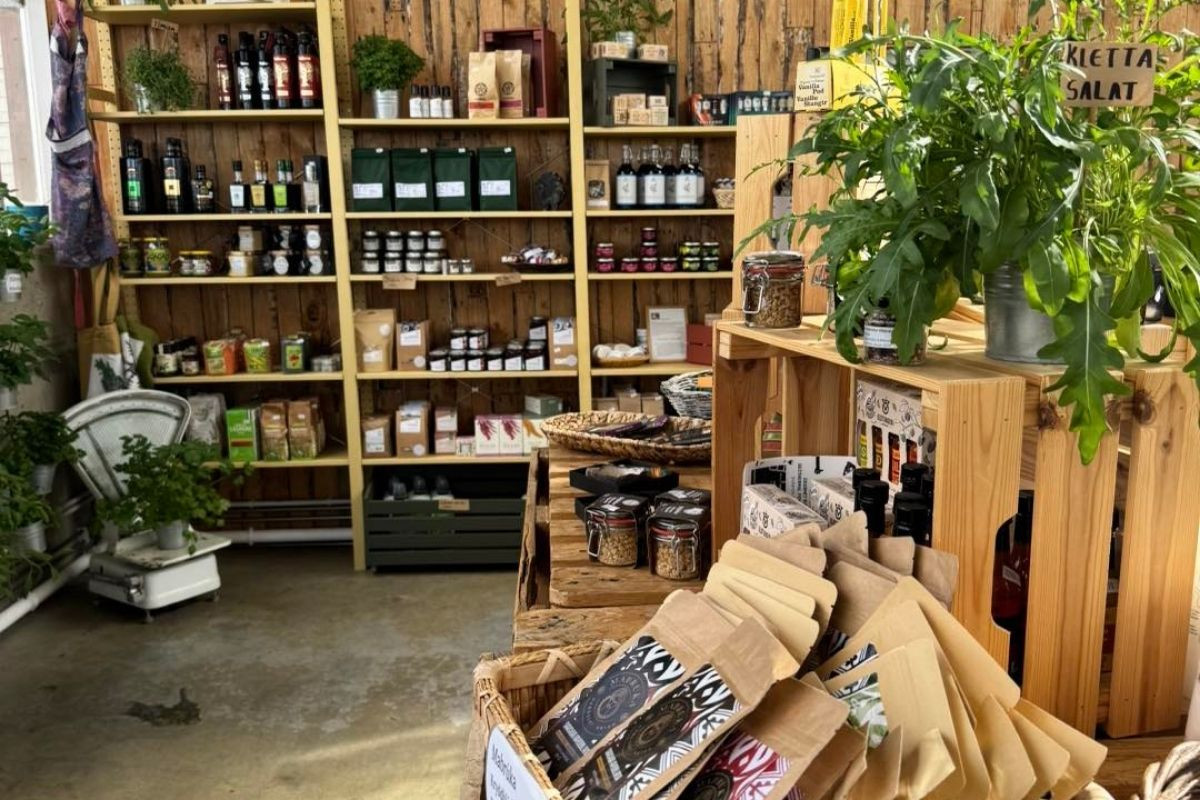 A vibrant display of organic and locally sourced products at Sólskinsbúðin, including bottled oils, packaged foods, and fresh greens, arranged on wooden shelving and crates.