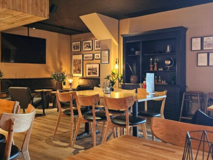 The interior of Public Deli Restaurant in Iceland, featuring modern wooden tables and chairs, comfortable lounge seating, framed artwork on the walls, and a large TV screen.