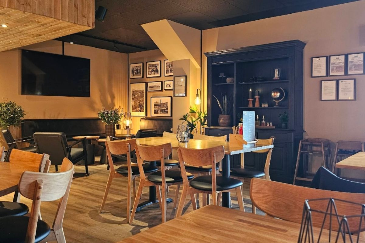 The interior of Public Deli Restaurant in Iceland, featuring modern wooden tables and chairs, comfortable lounge seating, framed artwork on the walls, and a large TV screen.