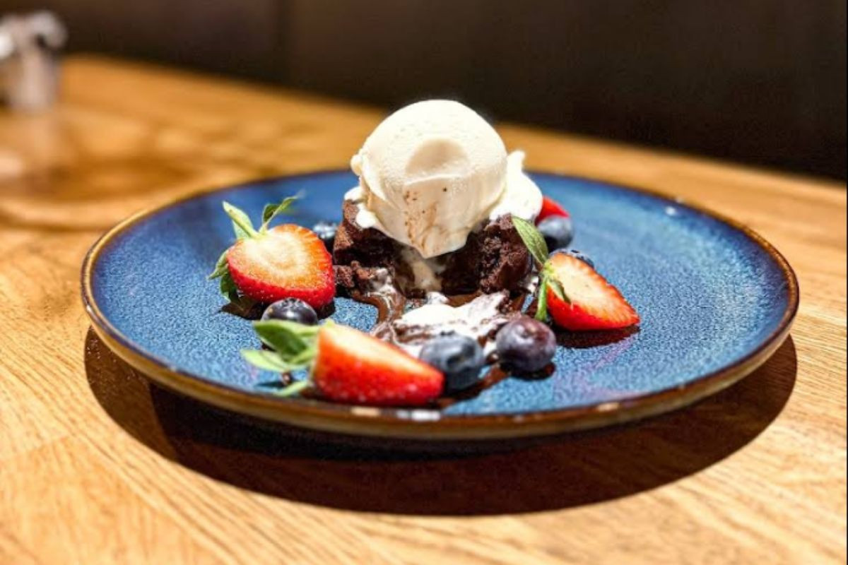 A decadent chocolate lava cake topped with vanilla ice cream, fresh strawberries, and blueberries on a blue plate, served at Public Deli Restaurant.