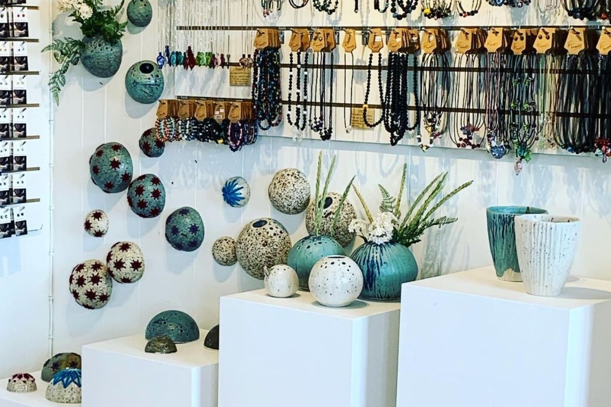 Interior view of Gallery Flói, an Icelandic artisan gift shop, displaying a variety of handmade items including ceramic vases and spherical art pieces on white pedestals, and numerous necklaces and bracelets hanging on a white wall.