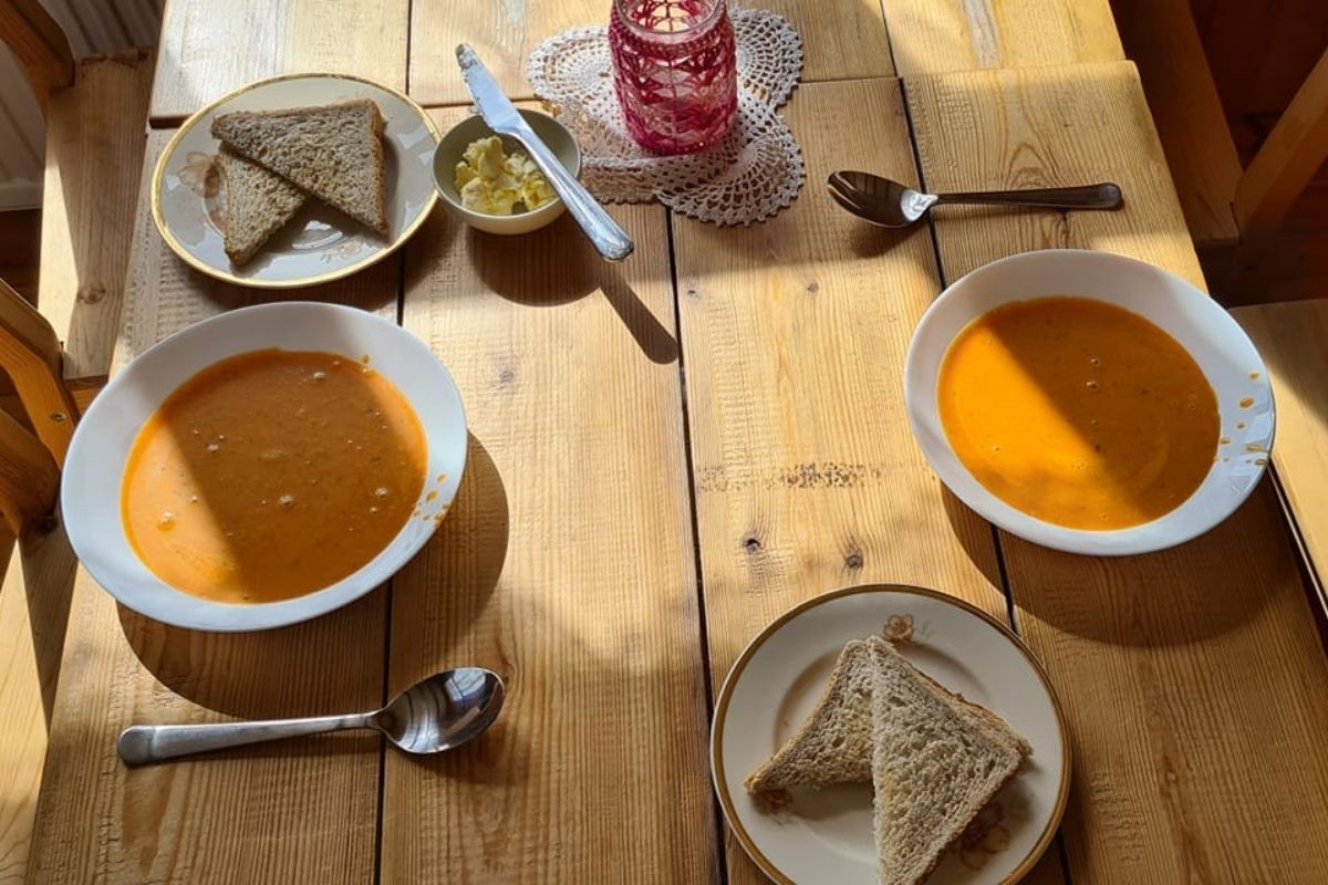 Two bowls of warm soup with accompanying toast and butter served on a sunlit wooden table at The Old Farmhouse Cafe in Iceland.