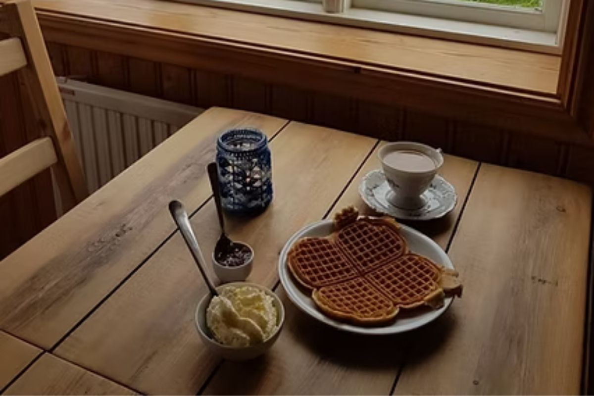 A plate of fresh, heart-shaped waffles with whipped cream and jam, and a cup of coffee on a rustic wooden table at The Old Farmhouse Cafe in Iceland.