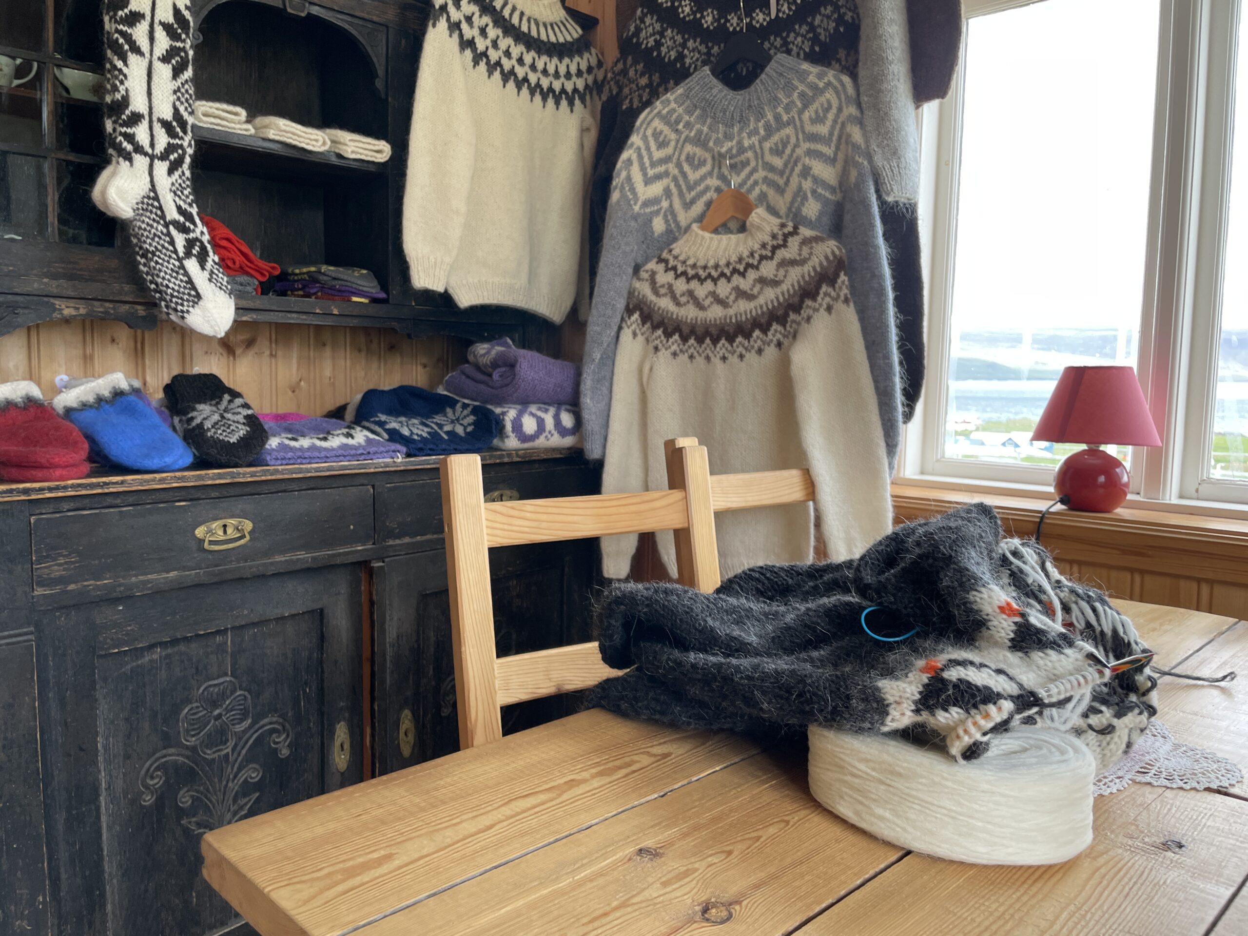 Traditional Icelandic wool sweaters (lopapeysa) and knitted goods displayed in a cozy room at Gamli bærinn - Brjánslæk, with knitting in progress on a wooden table.