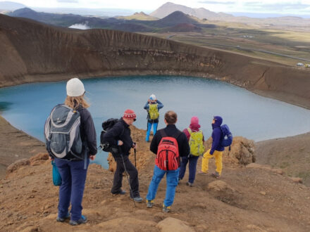 A group of people hiking near a vibrant blue lake surrounded by volcanic terrain.