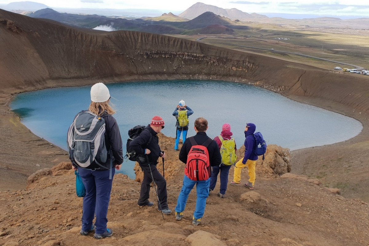 A group of people hiking near a vibrant blue lake surrounded by volcanic terrain.