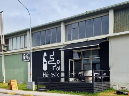 Exterior of Húsavík Öl brewery with a large black sign featuring its logo and a small outdoor patio.