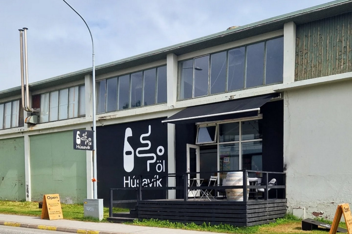 Exterior of Húsavík Öl brewery with a large black sign featuring its logo and a small outdoor patio.