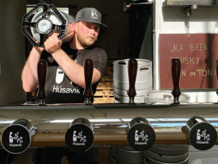 A man at a Húsavík brewery stand with beer taps and a menu.