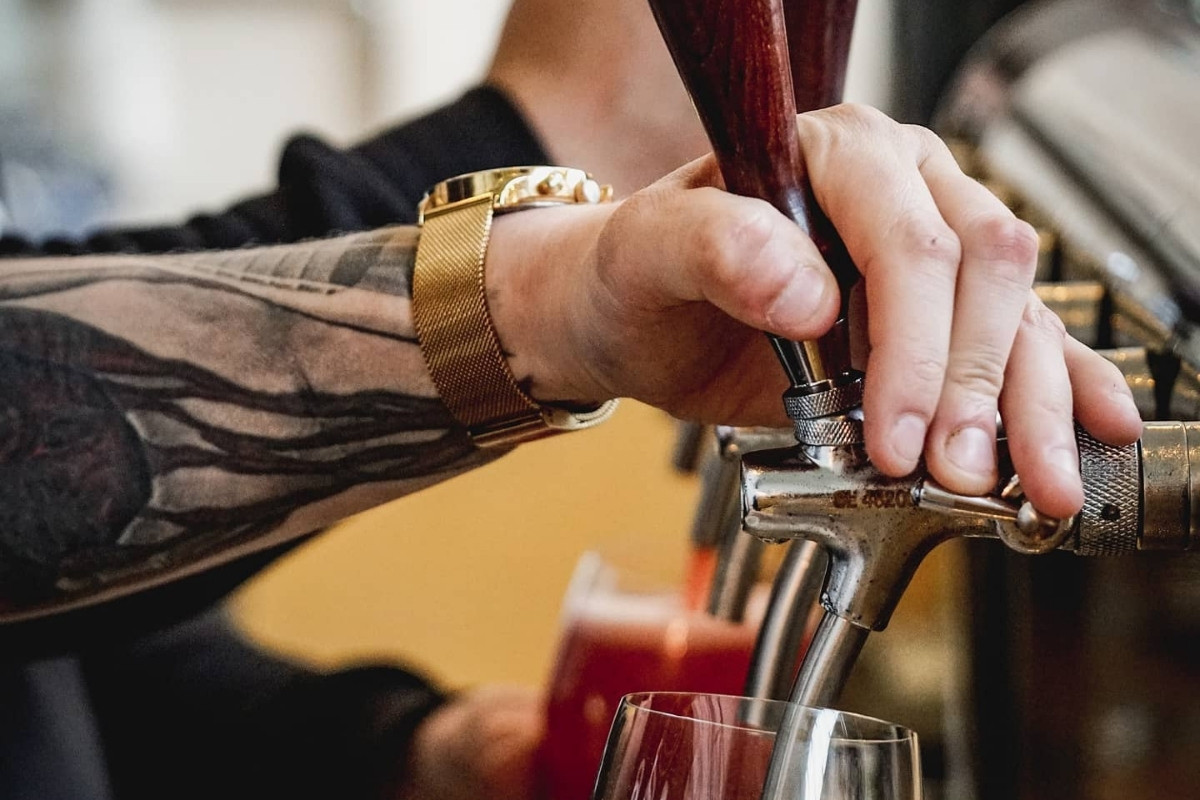 Close-up of a hand with a golden watch pouring a red beverage from a tap into a glass.
