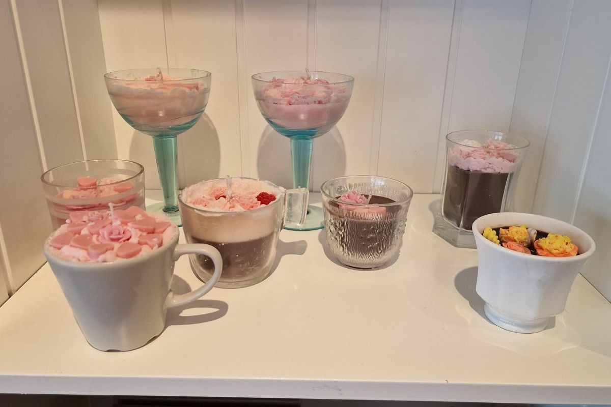 Assortment of decorative candles in Kertahúsið resembling drinks and desserts, including some with pink toppings, displayed on a shelf.