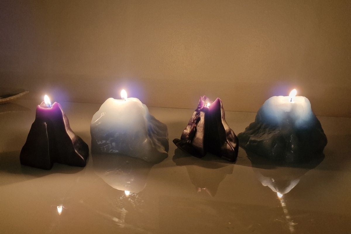 Four lit, irregularly shaped candles in purple and light blue, casting soft reflections.
