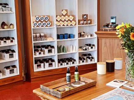 Kertahúsið, an Icelandic candle and gift shop, showcasing artisan candles, miniature house decor, and other boutique items on white shelving units and a wooden display table.
