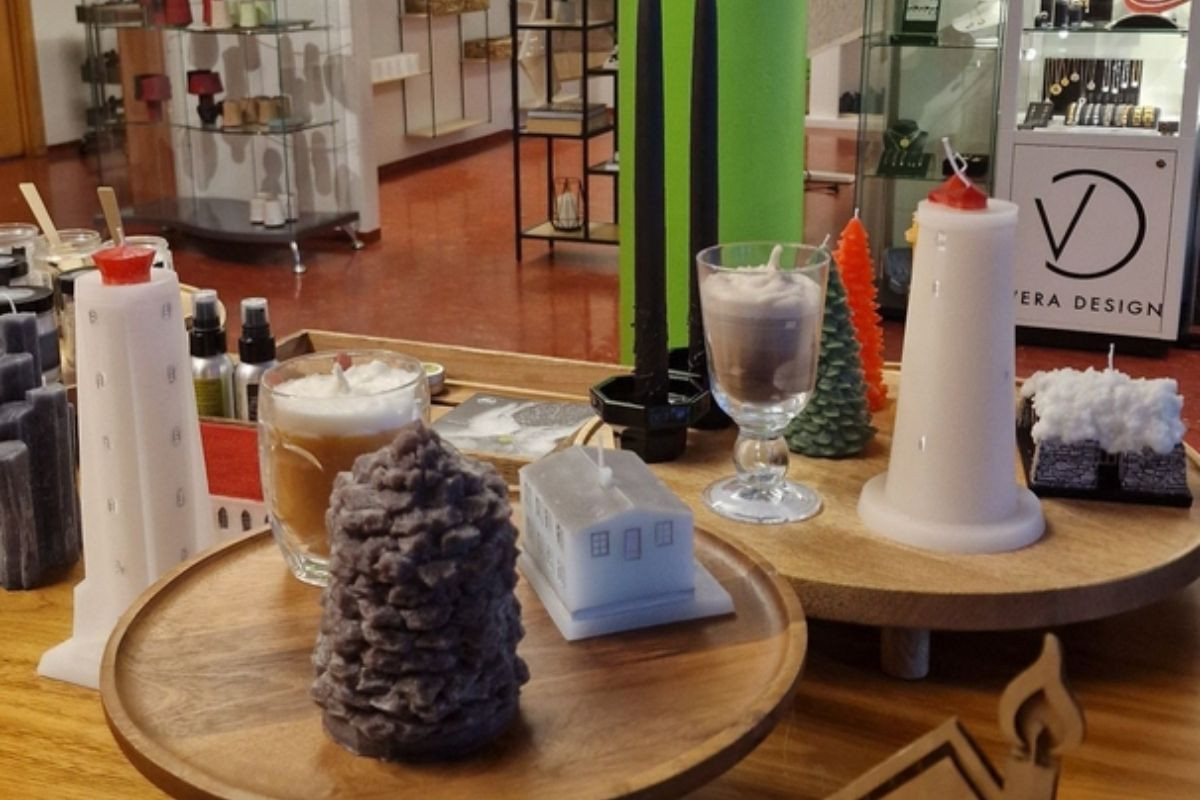 A variety of unique candles, including lighthouse shapes, a house, and textured designs, displayed on wooden trays in a store.