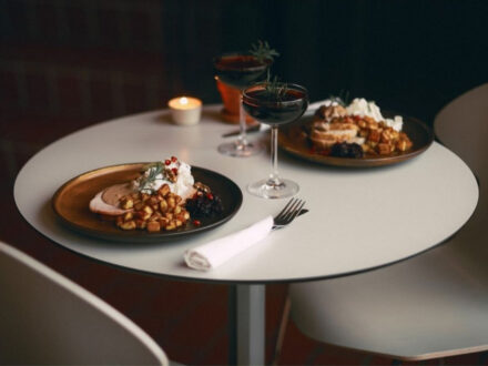 A round table with two plates of food, two wine glasses, and a lit candle.