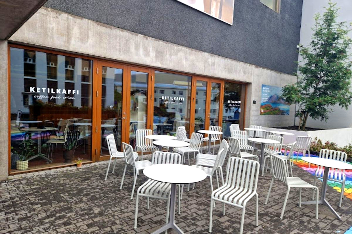 The exterior of Ketilkaffi cafe with an outdoor patio area filled with white tables and chairs.