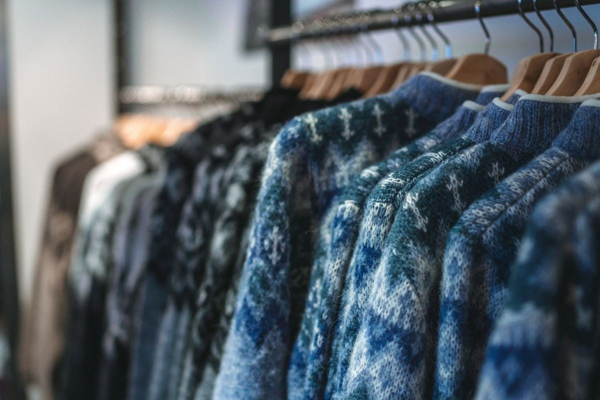 A close-up view of several Kidka knit sweaters on hangers, showcasing different patterns and colors.