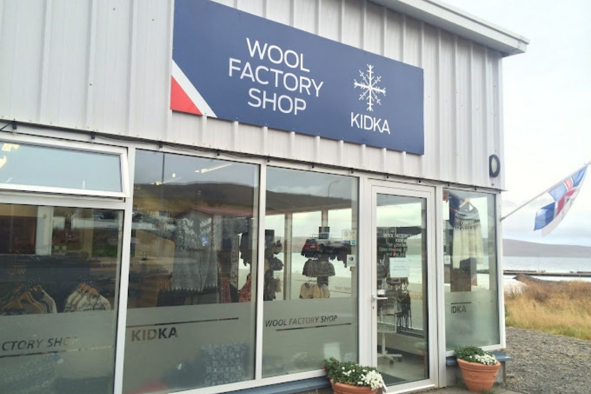 The exterior of the Kidka Wool Factory Shop, a white building with large windows and a blue sign.