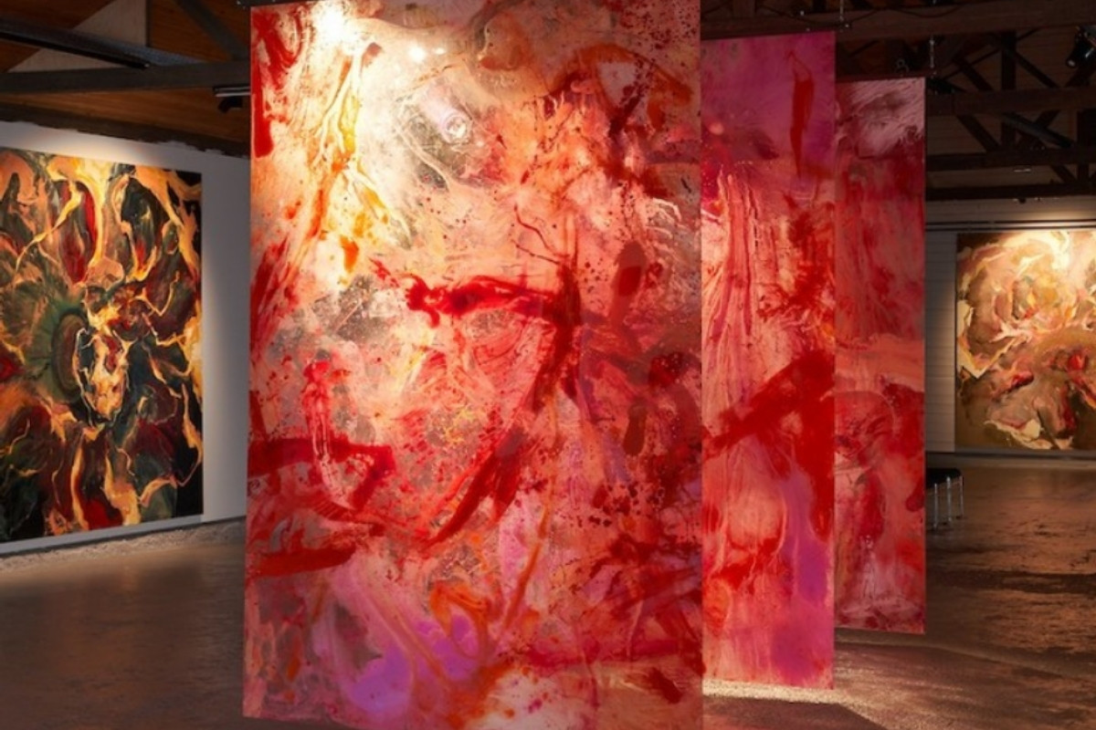 Abstract paintings dominated by shades of red, orange, and white, displayed on large panels in a gallery space.