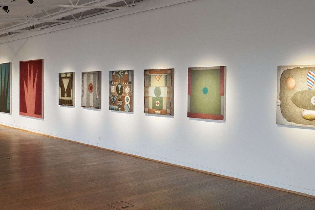 A series of framed abstract geometric paintings displayed on a white wall in an art gallery.