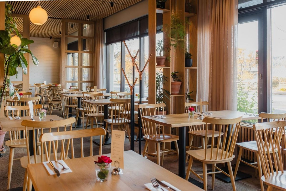 A cozy and well-lit dining area at Matkráin, with modern wooden furniture, elegant curtains, and natural light streaming through the windows.