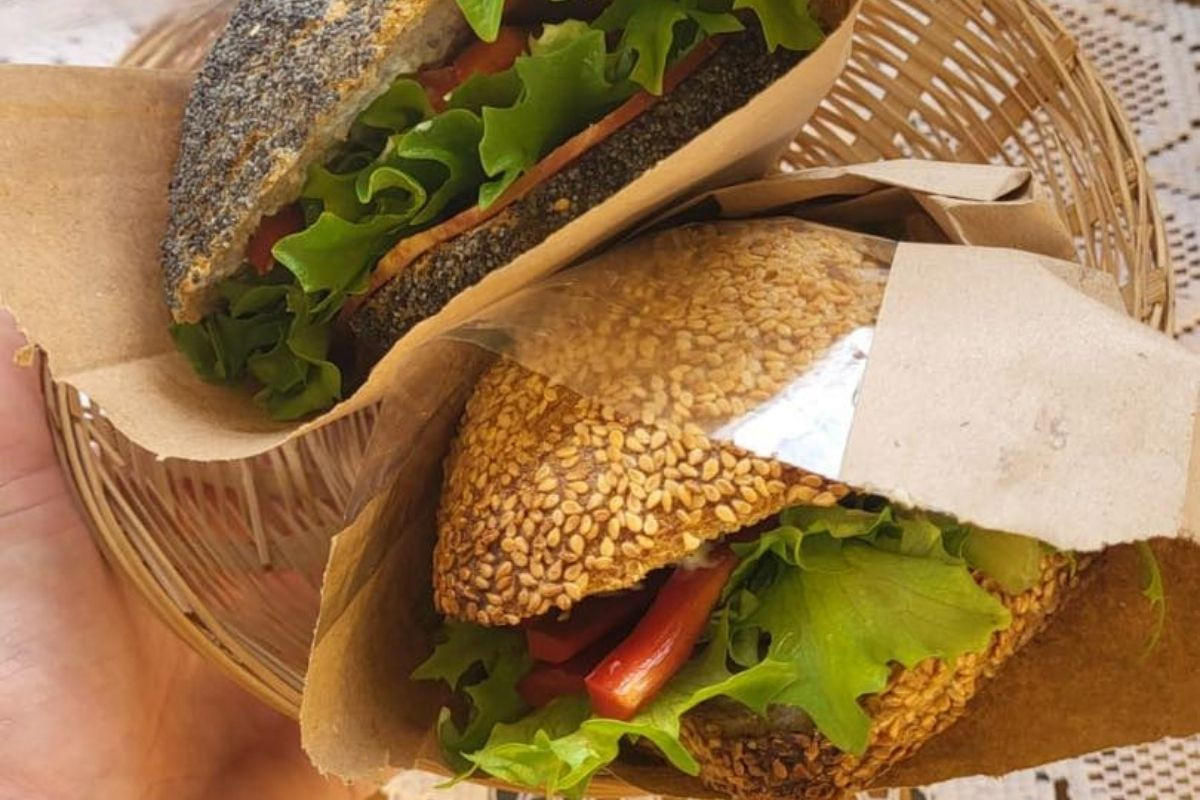 Two freshly made sandwiches, one on a poppy seed bun and one on a sesame seed bun, filled with lettuce and vegetables, wrapped in brown paper at Sólskinsbúðin.