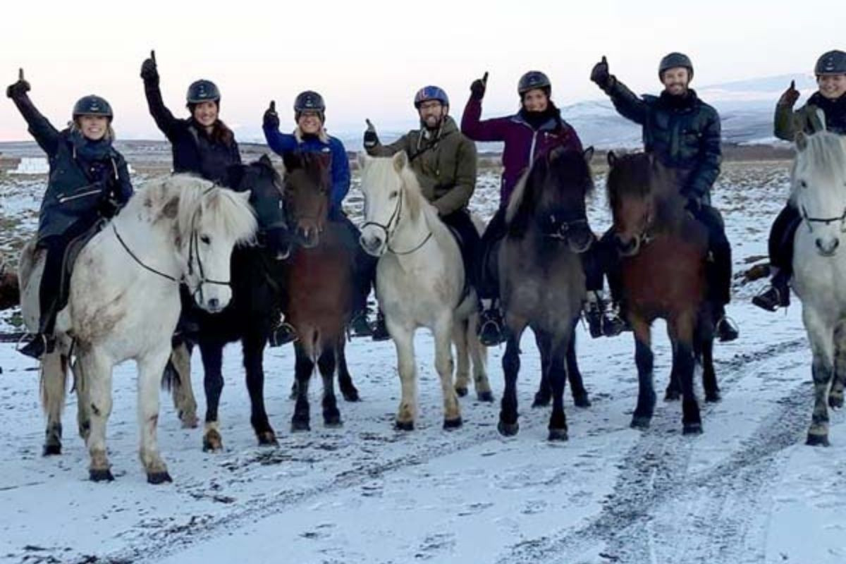 A group of people on Icelandic horses in a snowy landscape, giving thumbs up during a winter horse riding tour at Sturlureykir Horse Farm.