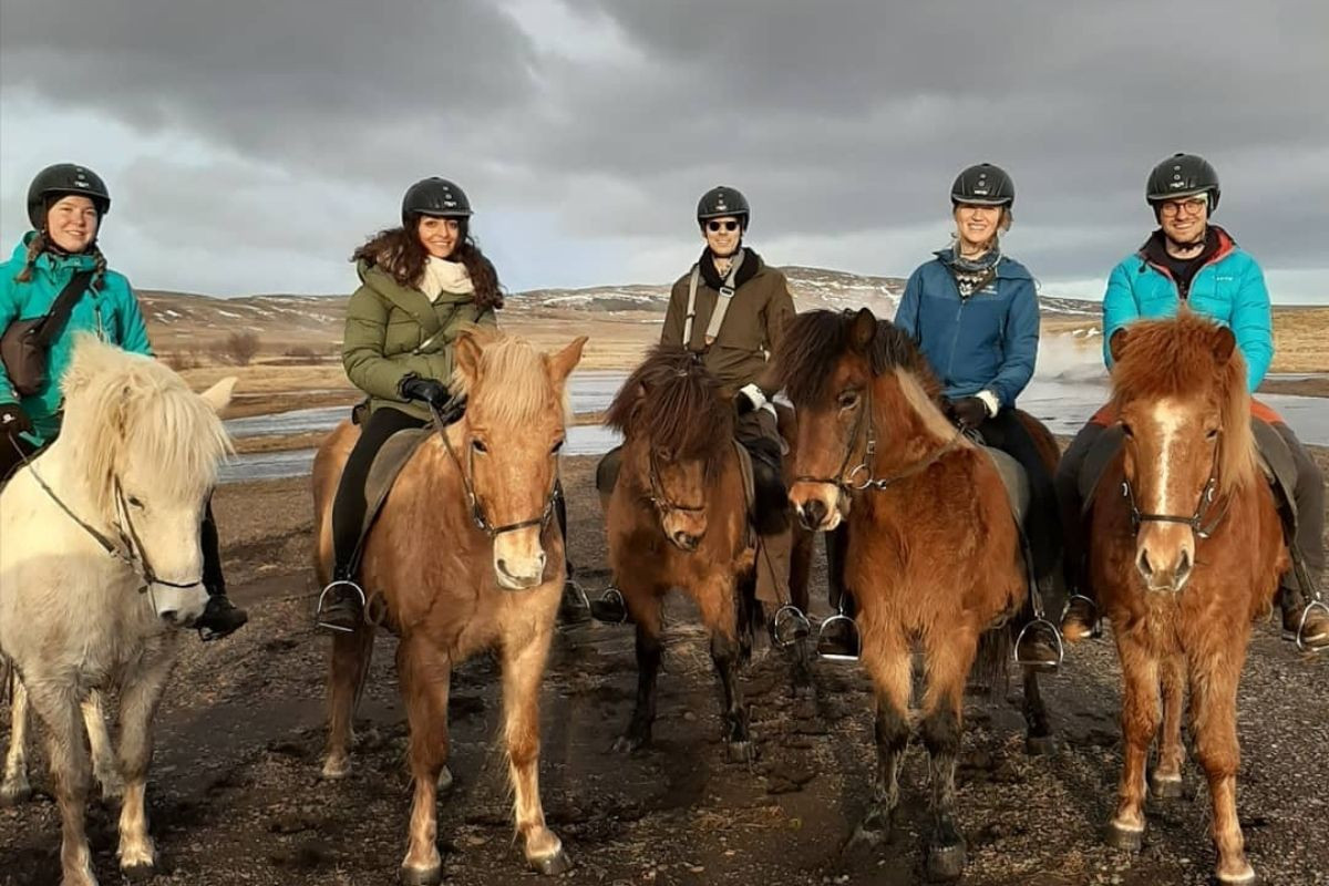 Five riders on Icelandic horses pose for a group photo during a horse riding tour at Sturlureykir Horse Farm in Iceland, with a rugged landscape in the background.