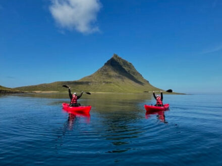 Vestur Adventures kayak tour in Iceland, featuring two kayakers in red boats with Kirkjufell mountain in the background.