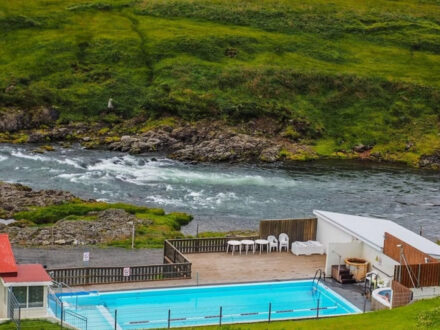 Selárdalslaug, a geothermal pool in Iceland, offers a unique bathing experience next to a river, with a small building and recreational area visible.